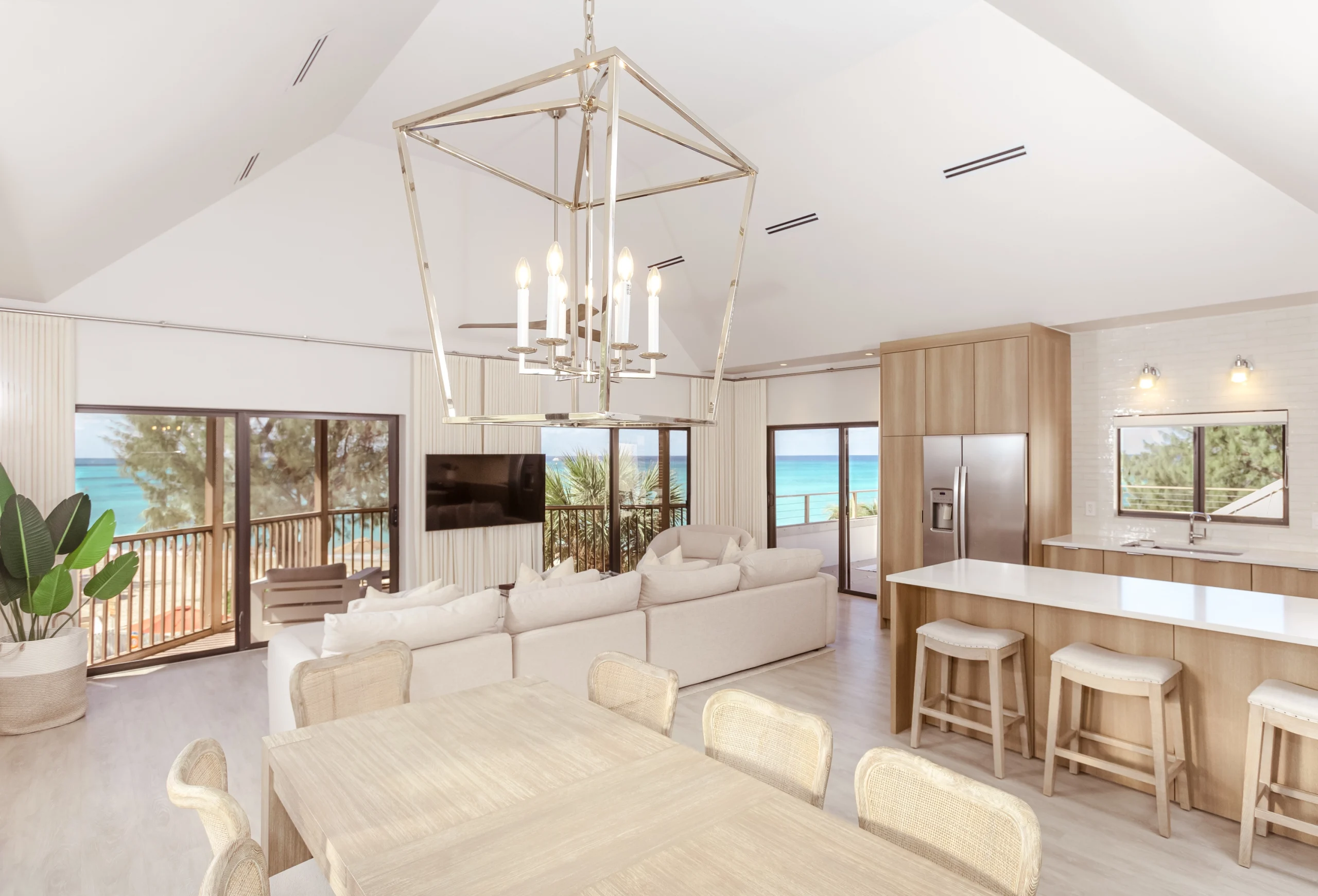 Open-plan living area with dining table, sectional sofa, kitchen island and ocean view through balcony doors.